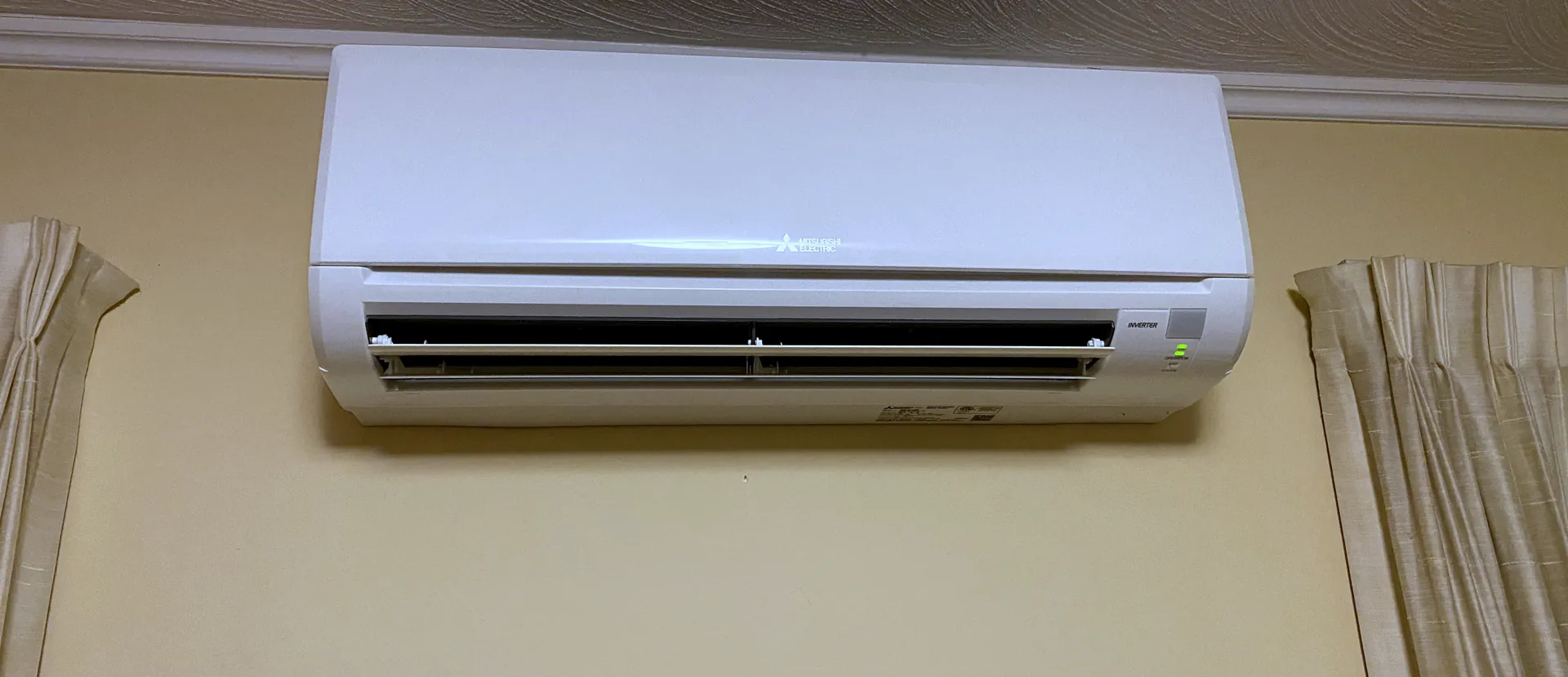 Mitsubishi Electric mini split indoor unit mounted on a living room wall between two curtained windows