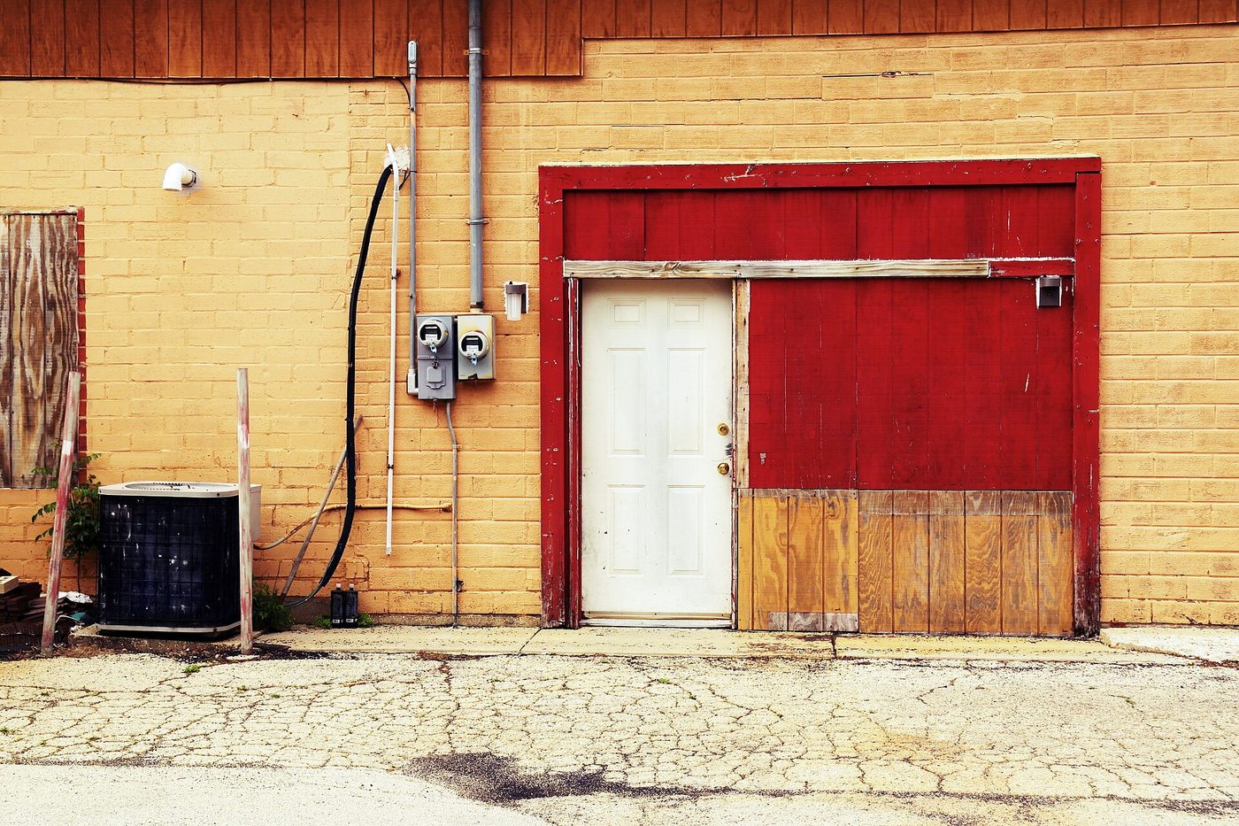 Older single-speed central air conditioner condenser sitting beside a building's electric meters